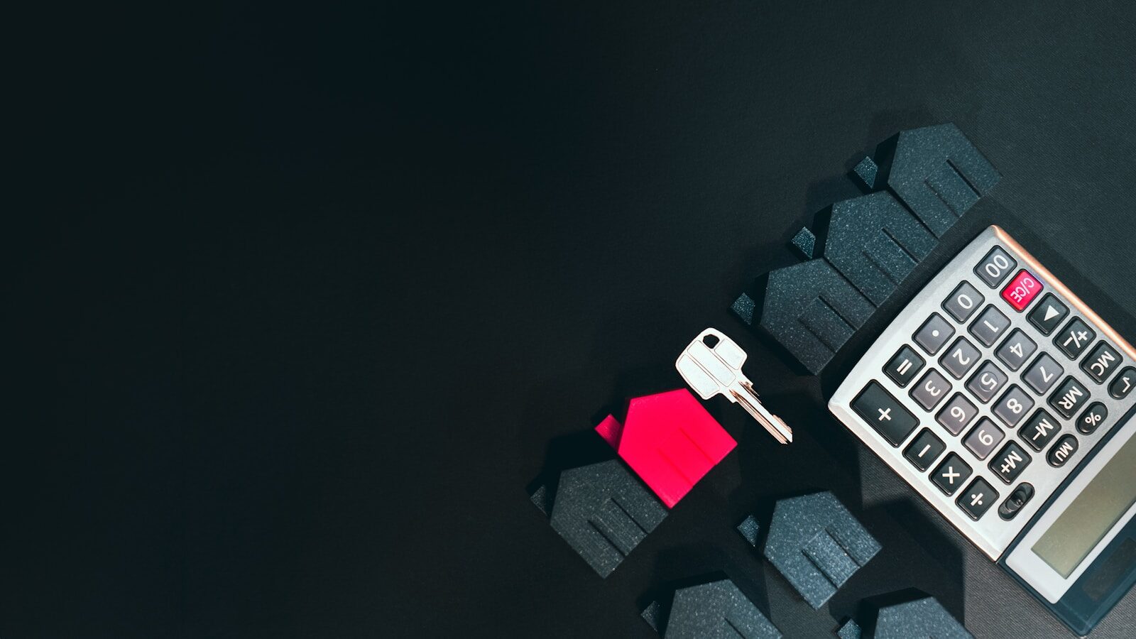 A silver key, a red house model, and a calculator on a black surface